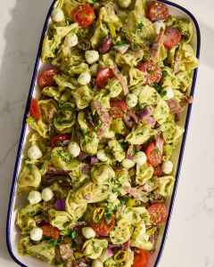 Pasta salad with tortellini, cherry tomatoes, olives, mozzarella balls, and herbs in a serving dish.