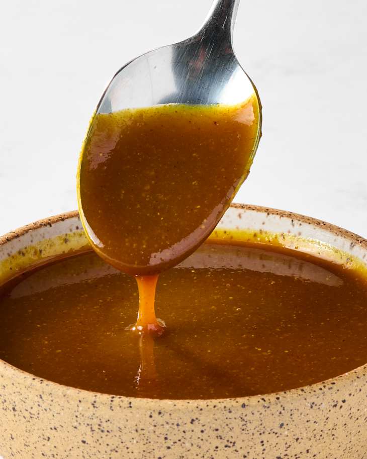 bowl of honey gold sauce with some dripping off of a spoon
