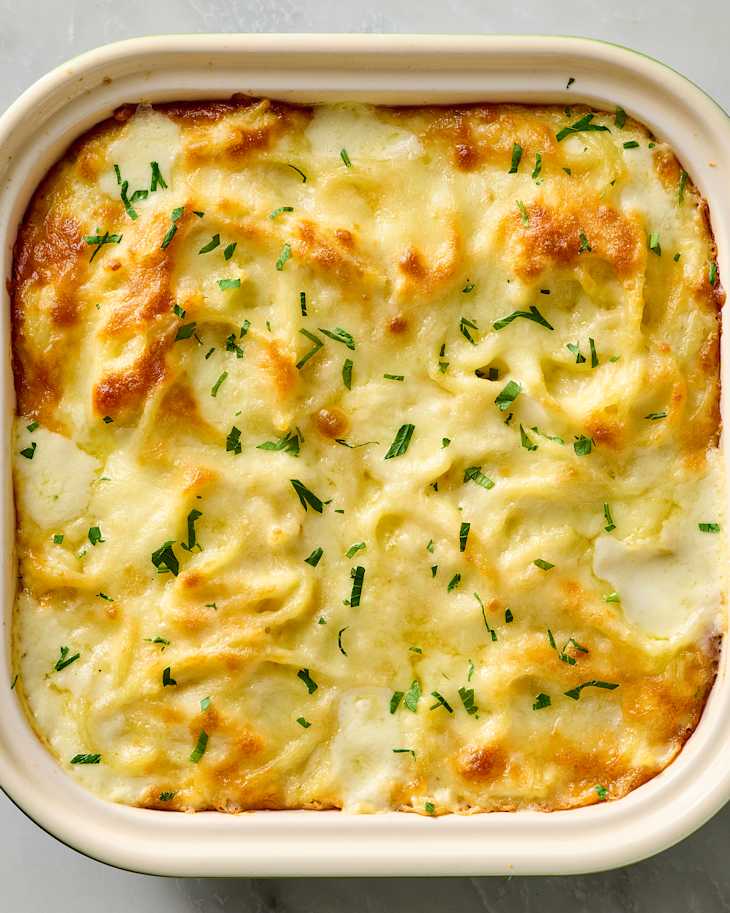 Creamy baked spaghetti topped with melted cheese and fresh herbs in a square dish.