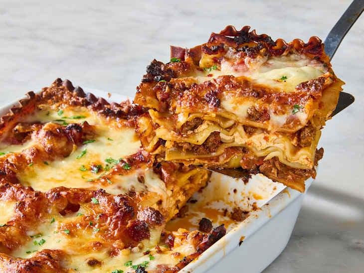 A serving of lasagna being lifted from a white baking dish, featuring layers of pasta, meat, and melted cheese.